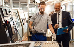 Manual worker and engineer checking quality of manufactured component - small