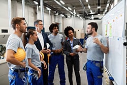 Manufacturing worker communicating with company leaders and his coworkers during business presentation in a factory