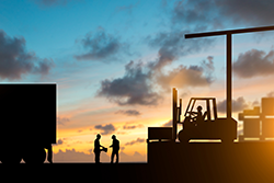 Silhouette of inspector examining the waybill with forklift and truck bringing up the goods